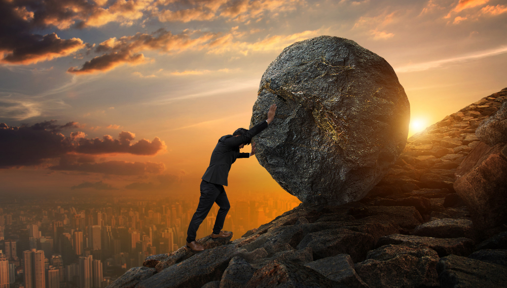 Image with business man pushing big stone up hill representing resilience.